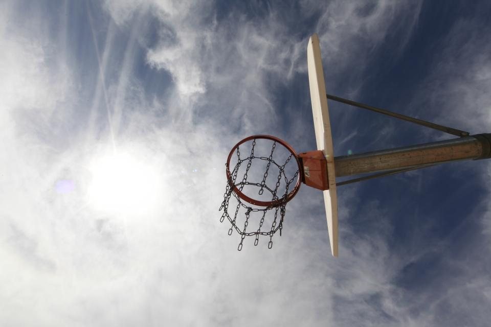 Looking up at a basketball hoop and net against a bright, cloudy sky