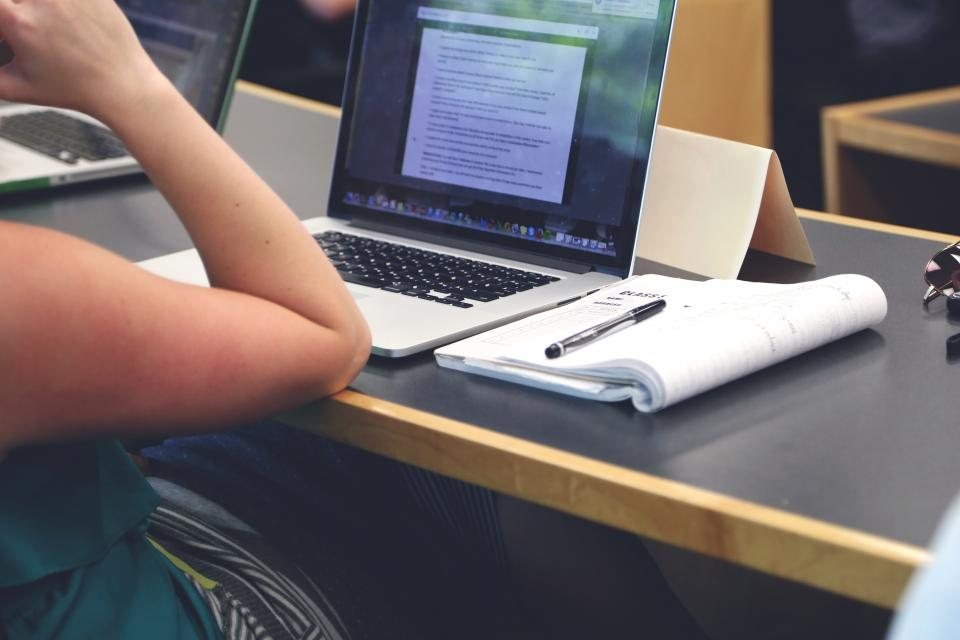 A student working on a laptop with an open notebook and pen on the desk
